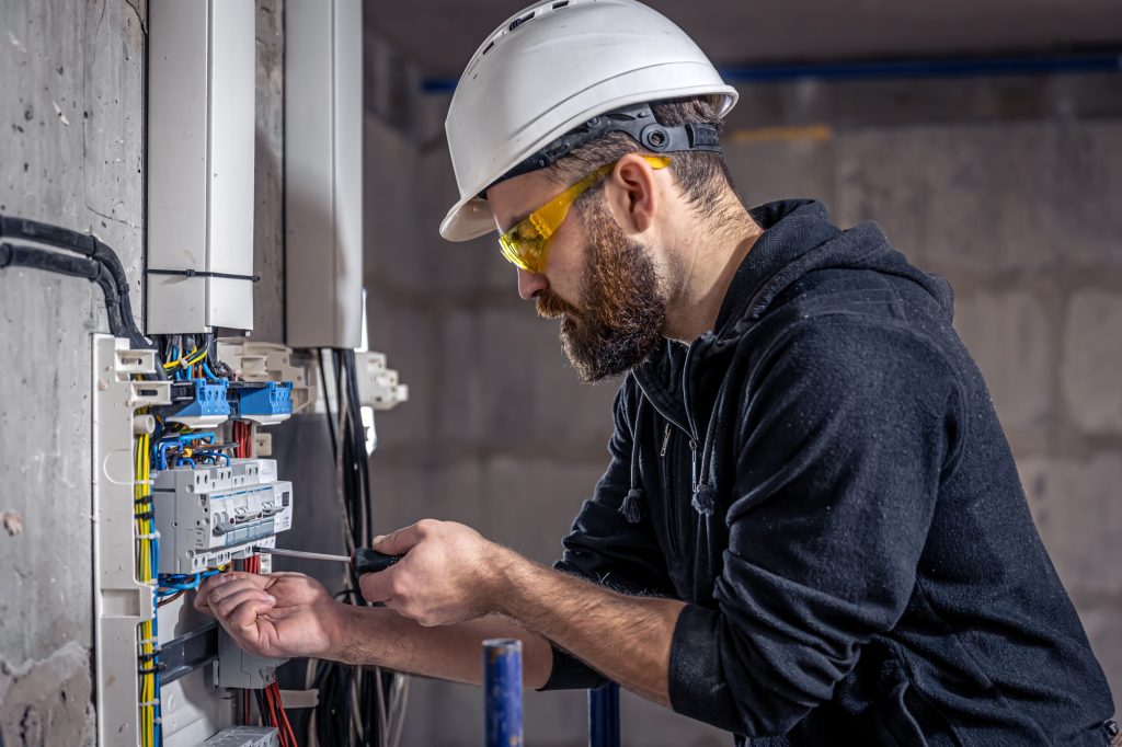 Reliable Electrical Services in Lynnwood & Snohomish County A male electrician works in a switchboard with an electrical connecting cable.